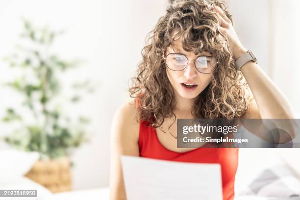 shocked young woman reading a letter she received from a lawyer, office or utility bill. - brief stock-fotos und bilder