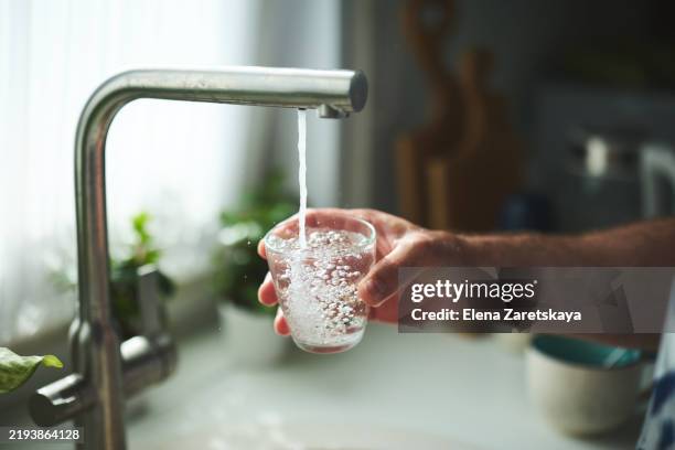 hand holding glass under tap for fresh drinking water at home - fontein stockfoto's en -beelden