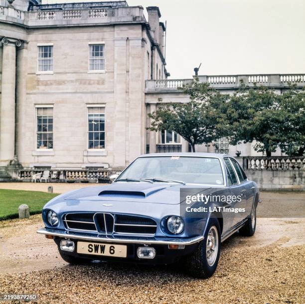Blue Aston Martin Lagonda series I parked on gravel outside Tyringham Hall, Buckinghamshire. Circa October 1974.