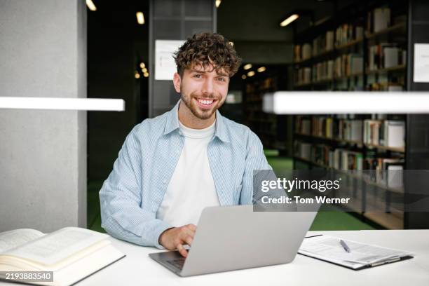 portrait of a happy student using laptop at library study desk - laptop sitting on stack of books stock pictures, royalty-free photos & images