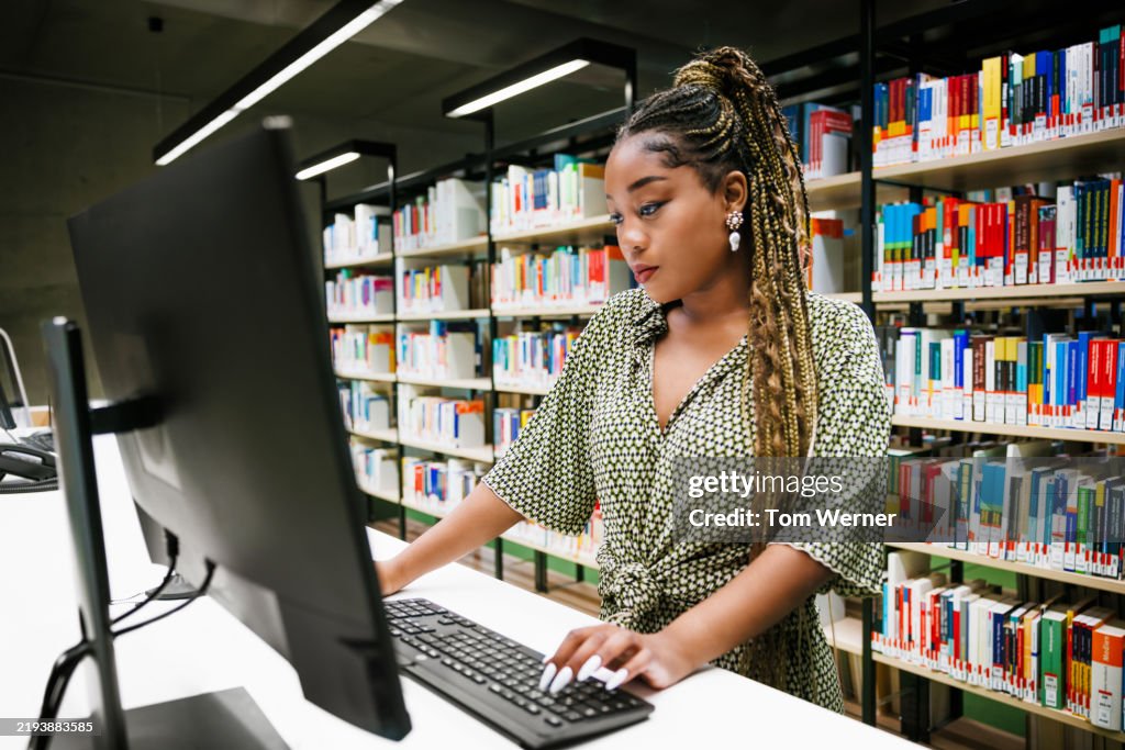Young Female Student Analyzing Work on a Computer in a Modern Library