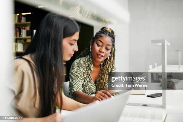 collaborative learning session between two female students in a modern library environment - aprender fotografías e imágenes de stock