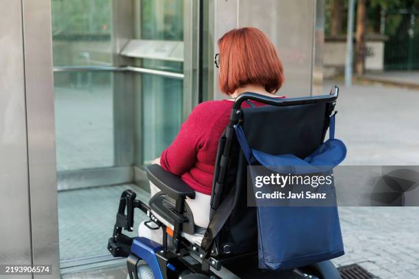 rear view of a red-haired woman using electric wheelchair waiting for elevator access, promoting accessibility and inclusion for people with disabilities - hiss bildbanksfoton och bilder
