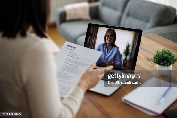 frau, die an einem virtuellen vorstellungsgespräch teilnimmt, während sie ihren lebenslauf in der hand hält - bewerbungsformular stock-fotos und bilder