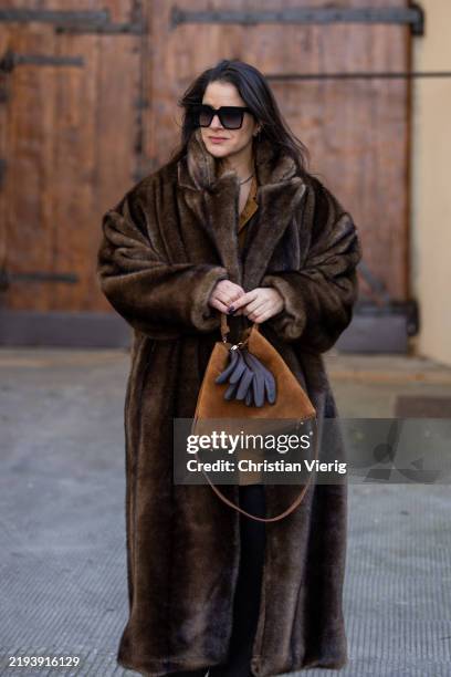 Gili Biegun wears fur coat, suede bag, shirt, wide leg denim jeans, white top during Pitti Immagine Uomo 107 on January 14, 2025 in Florence, Italy.