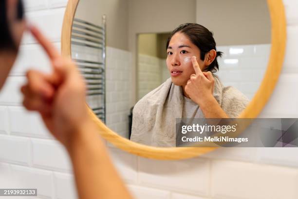 young man apllying facial creme on his face - man wipes face stock pictures, royalty-free photos & images