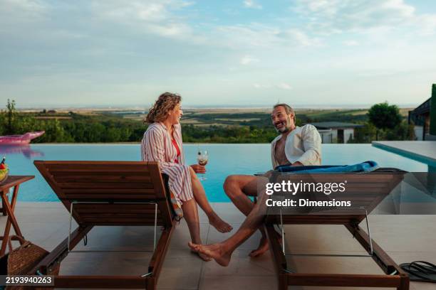coppia che si gode un drink rilassante a bordo piscina a sfioro con vista sulla campagna panoramica - bordo piscina foto e immagini stock