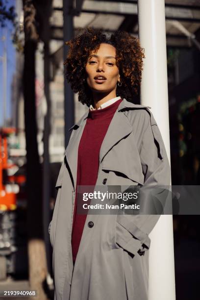 modische frau in grauem mantel, die an einem sonnigen tag posiert im freien - trenchcoat stock-fotos und bilder
