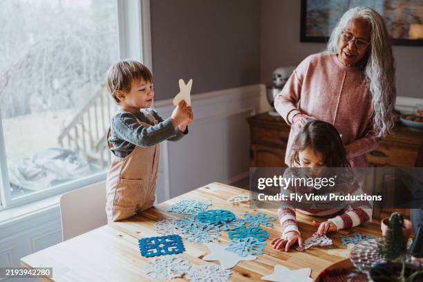 pacific islander senior woman cutting out paper snowflakes with her grandchildren - art and craft stock pictures, royalty-free photos & images