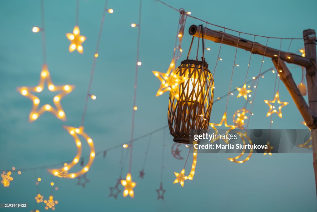Magical night sky with star and moon lantern string lights for romantic decor and celebrations.Lighting decor elements at a party outdoors. Cozy lights lanterns and light garland background.
