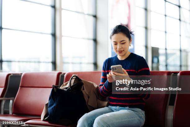 asian young woman with suitcase using smartphone while waiting for her flight at airport terminal. asian businesswoman on business travel. lifestyle and technology. travel and vacation concept. red series. - travel insurance stock pictures, royalty-free photos & images