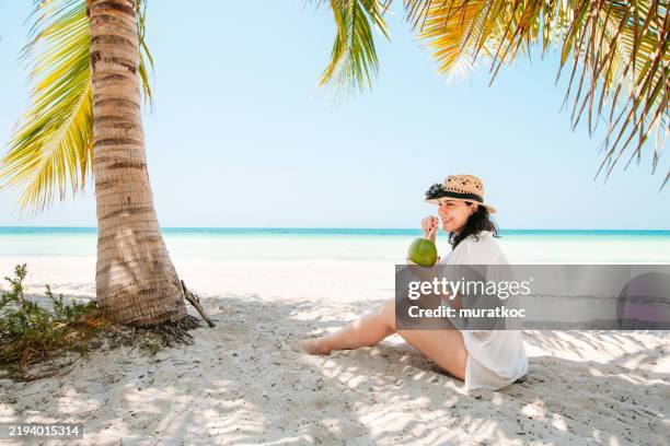 mujer joven que disfruta de la bebida de coco en la playa con palmera y vista al mar - caribe fotografías e imágenes de stock
