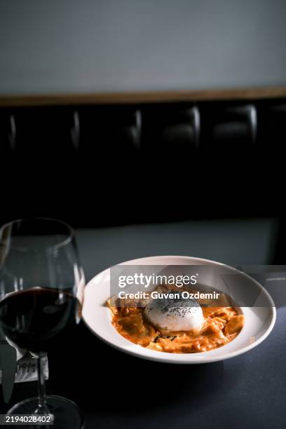 gros plan sur les pâtes pappardelle à la burrata et à la sauce tomate servies sur une assiette blanche, accompagnées d’un verre de vin rouge dans un élégant restaurant italien, ambiance culinaire chaleureuse et sophistiquée, cuisine italienne gast - stylisme culinaire photos et images de collection