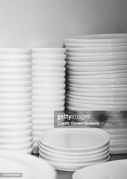 stacked white ceramic plates in a professional restaurant kitchen, minimalist monochrome composition highlighting clean tableware and organized dining essentials - serviesgoed stockfoto's en -beelden
