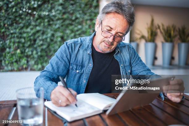 mature man studying with notebook and tablet at outdoor patio table - arranging stock pictures, royalty-free photos & images