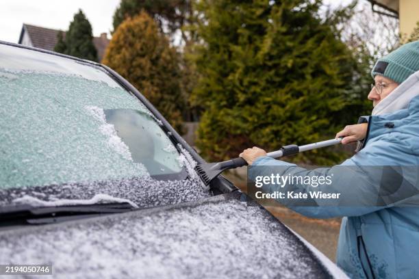 senior man wearing winter clothes and cleaning frost and snow from a car's windshield. - eiskratzer stock-fotos und bilder