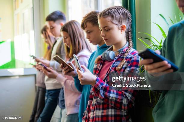 teenage students are standing in the school hallway, all looking at their phones. - smartphone stock pictures, royalty-free photos & images