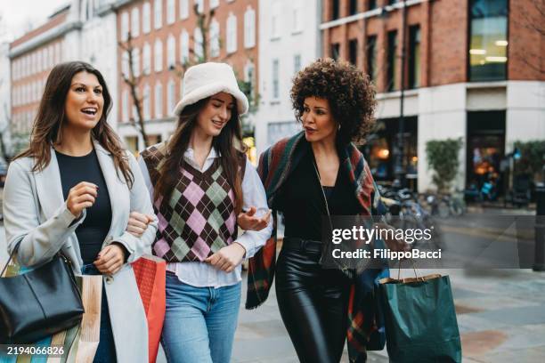 three cheerful female friends walking and talking on a shopping spree, carrying shopping bags - free shopping spree stock pictures, royalty-free photos & images