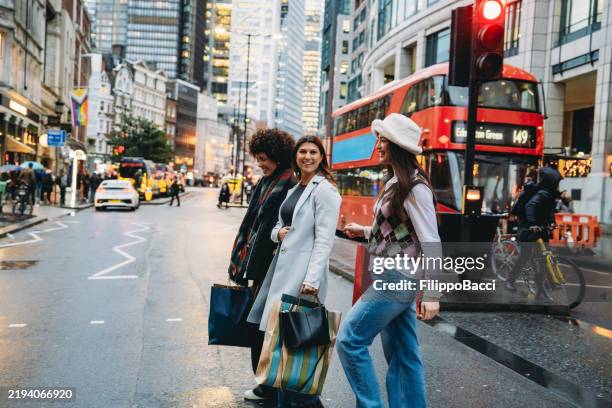 tres mujeres jóvenes que caminan en el paso de peatones en londres con bolsas de compras - london fotografías e imágenes de stock