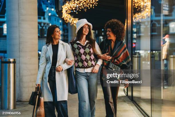 three young women walking and talking after christmas shopping spree - holiday spirit stock pictures, royalty-free photos & images
