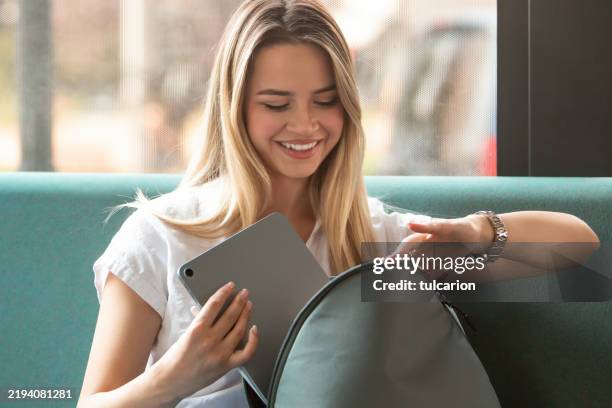 woman taking tablet from backpack with a smile - university gate stock pictures, royalty-free photos & images
