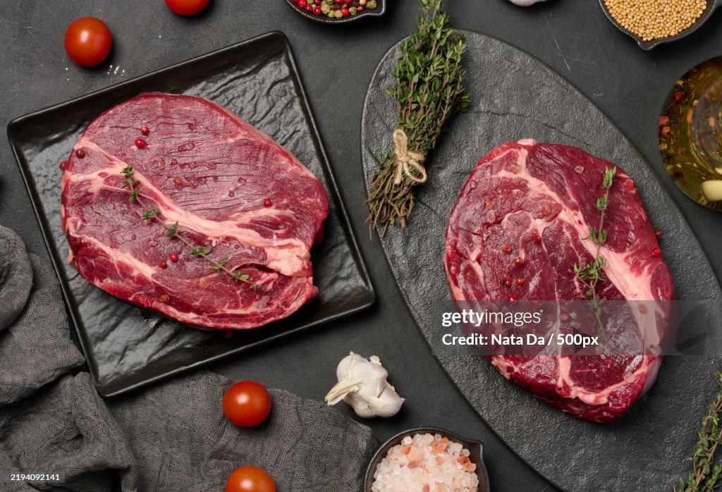 A wooden board holds a raw chuck eye roll steak,Complemented by Himalayan salt,Thyme sprigs,And peppercorns