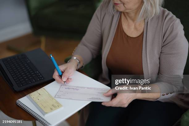 donna che firma un assegno a una scrivania con laptop e blocco note - busta paga foto e immagini stock