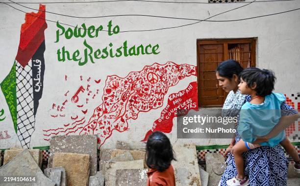 An Indian woman with her children walks next to a mural showing solidarity with the Palestinian resistance painted outside a house in a slum in...