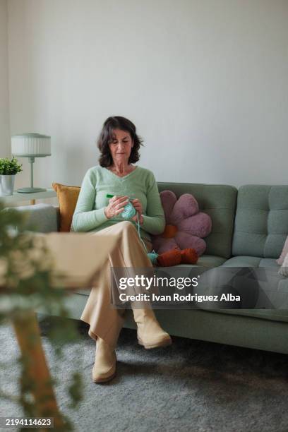 senior woman knitting on sofa in cozy living room - wool carpet stock pictures, royalty-free photos & images