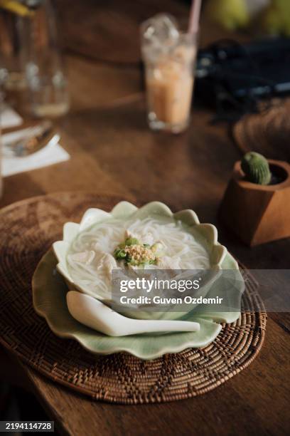 traditional thai guay teaw gai noodle soup served in an elegant lotus-shaped bowl, garnished with green onions and fried garlic, on a woven mat, highlighting authentic thai flavors - chinese food stock pictures, royalty-free photos & images