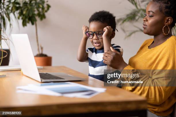 mother helping son with eyeglasses while using laptop at home - take your child to work day stock pictures, royalty-free photos & images