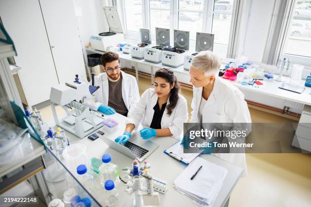 three scientists are engaged in a collaborative discussion around a laptop in a laboratory - bioquímica imagens e fotografias de stock