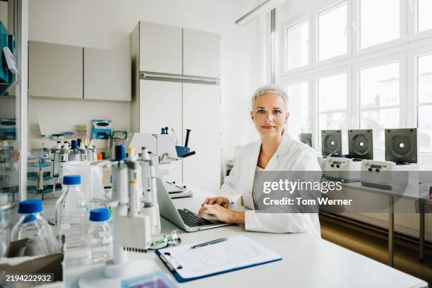 portrait of a female scientist typing on a laptop while sitting at a laboratory desk - alleen één oudere vrouw stockfoto's en -beelden