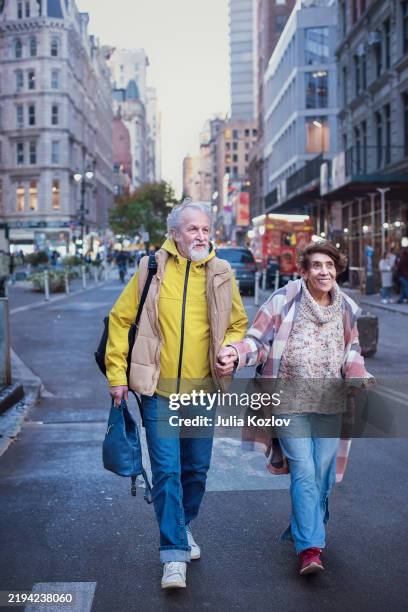 stroll through manhattan streets. senior couple holding hands while exploring new york city - couple crossing street stock pictures, royalty-free photos & images
