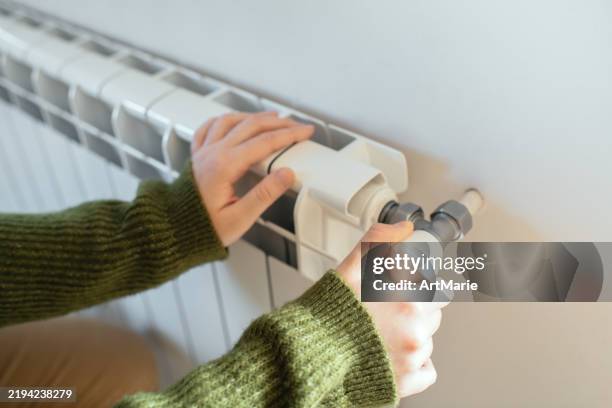 young woman trying to warm near a radiator in winter - turner syndrome stock pictures, royalty-free photos & images