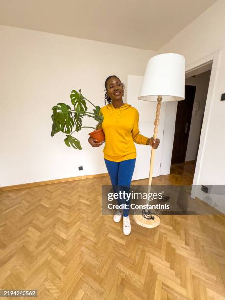 mujer negra emocionada que entra en un nuevo espacio con lámpara y planta en maceta - tomado desde un teléfono móvil fotografías e imágenes de stock