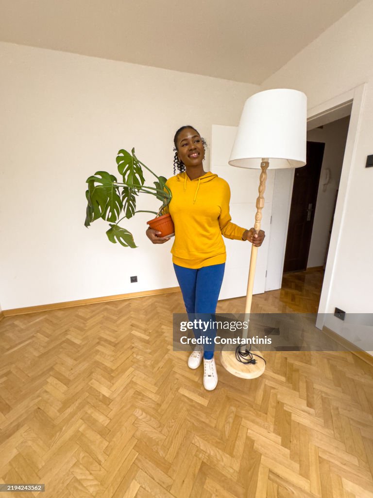 Femme noire excitée entrant dans un nouvel espace avec une lampe et une plante en pot