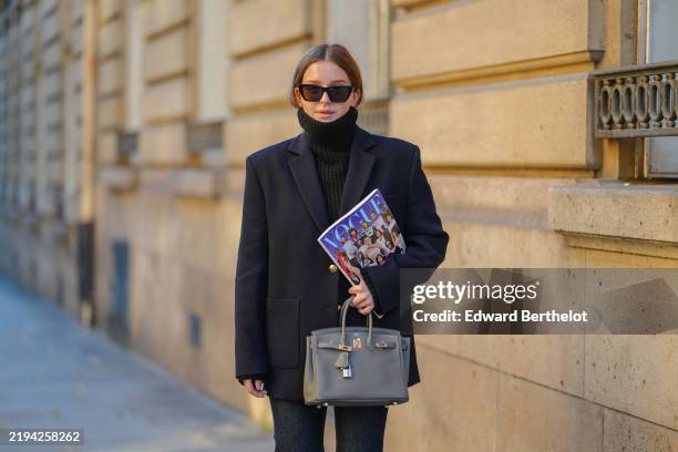 Diane Batoukina wears black sunglasses, a black cashmere Zara turtleneck pullover, a dark blue blazer jacket, a grey leather Birkin Hermes bag, black...