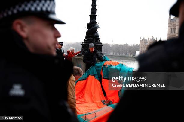 Police officers watch climate activists as they prepare to unveil a giant banner reading "Trump: Climate Genocide" on the Southbank opposite to the...