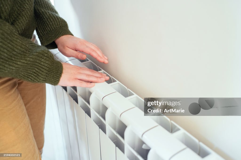 Young woman trying to warm near a radiator in winter