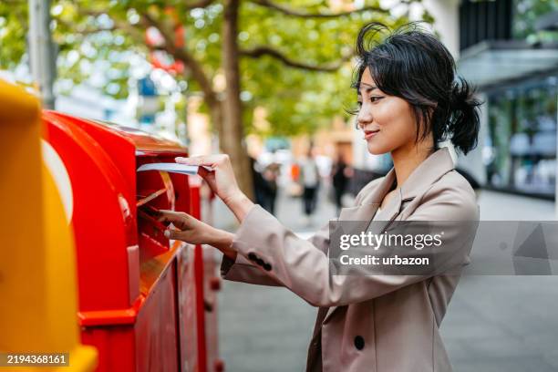 young asian businesswoman mailing a letter while on the street in sydney in australia - sending stock pictures, royalty-free photos & images