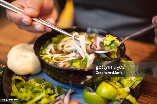 man eating vietnamese dish pho soup in a cafe - vietnamese coriander stock pictures, royalty-free photos & images