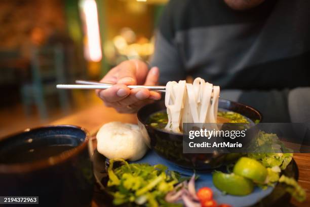 man eating vietnamese dish pho soup in a cafe - vietnamese coriander stock pictures, royalty-free photos & images