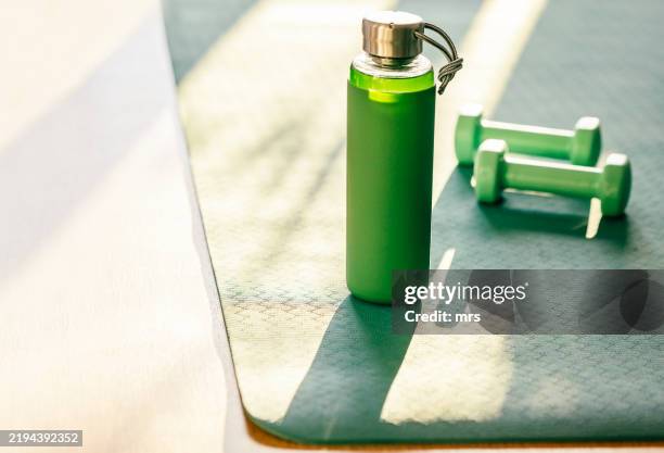 water bottle and dumbbells on yoga mat - fitnessapparatuur stockfoto's en -beelden