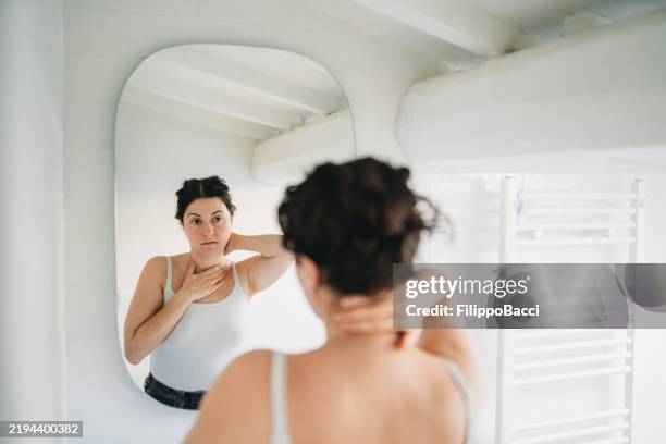 junge frau, die ihren hals im spiegel im badezimmer untersucht - hals stock-fotos und bilder
