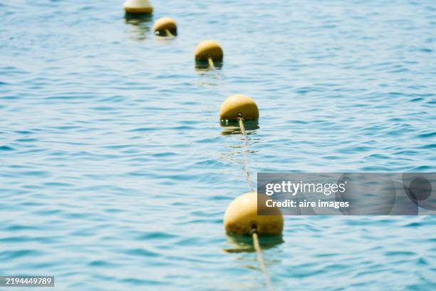 yellow buoys floating on a calm sea creating a dividing line - buoy stock pictures, royalty-free photos & images