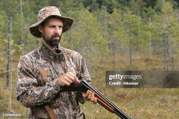 hunter loads shotgun in forest - man in camouflage gear prepares for hunt during autumn season - caça imagens e fotografias de stock