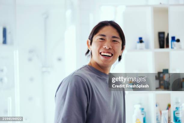 smiling young man in a bright bathroom setting with toiletries - nachtkleding stockfoto's en -beelden