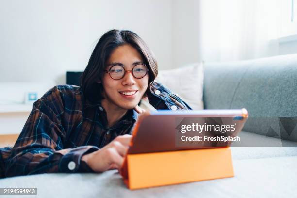 giovane adulto sorridente che usa il tablet sul divano in un ambiente domestico rilassante - occhiali da lettura foto e immagini stock
