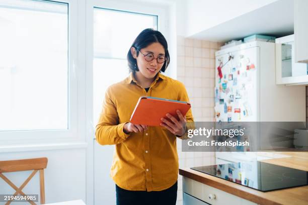 hombre en la cocina brillante usando la tableta y sonriendo mientras lee - camisa de colores fotografías e imágenes de stock